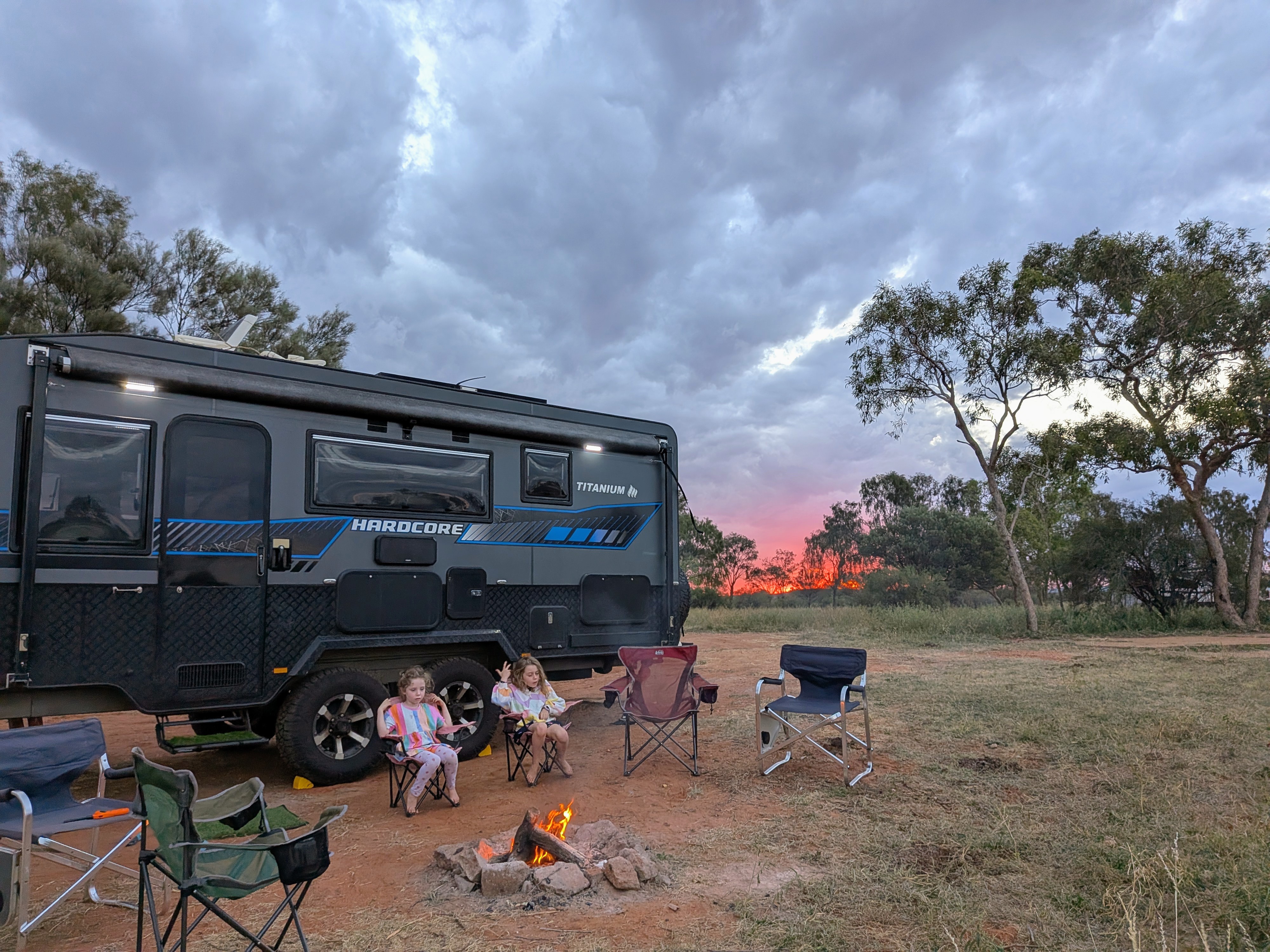 The girls by the campfire with TITANIUM HARDCORE and a red sunset behind
