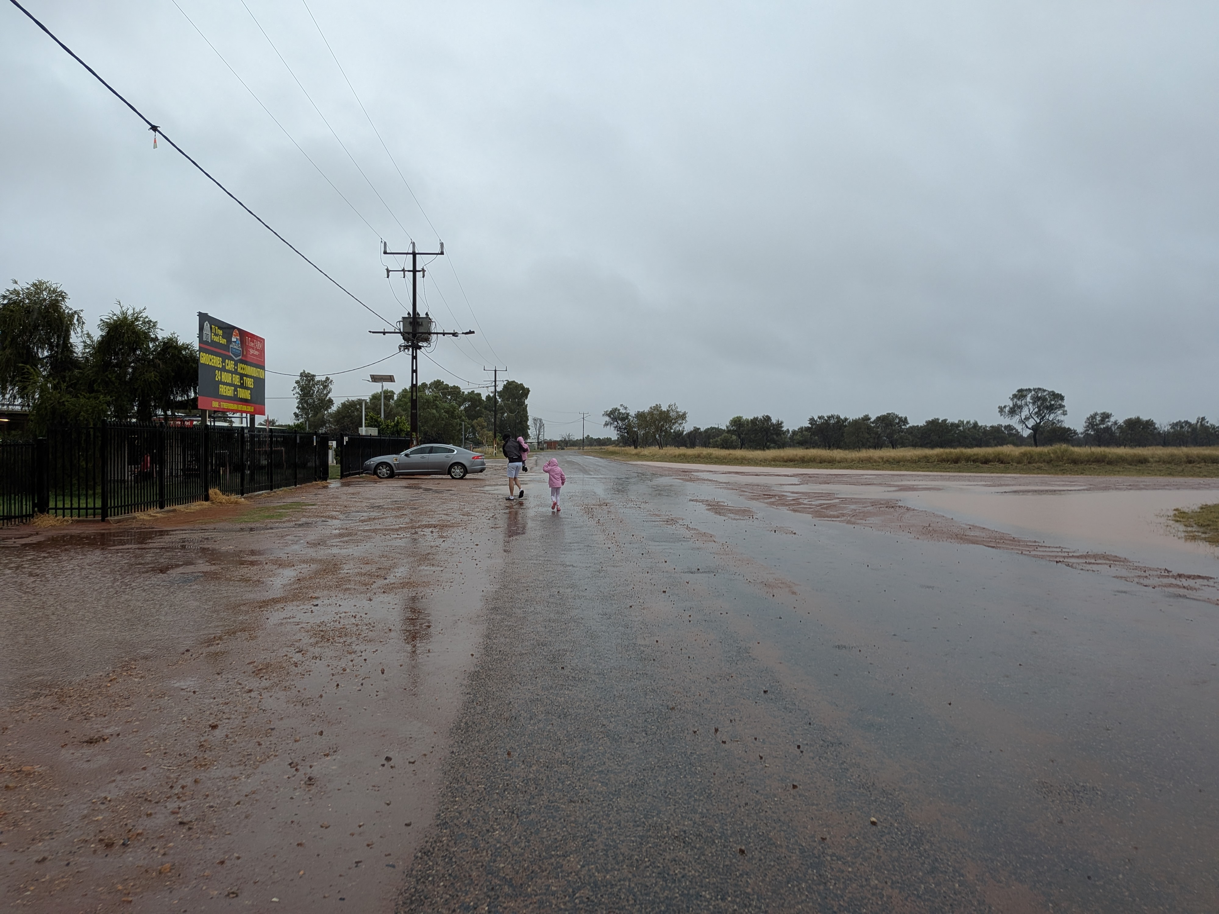 Dylan and Leah walking across the wet road at Ti Tree in the rain