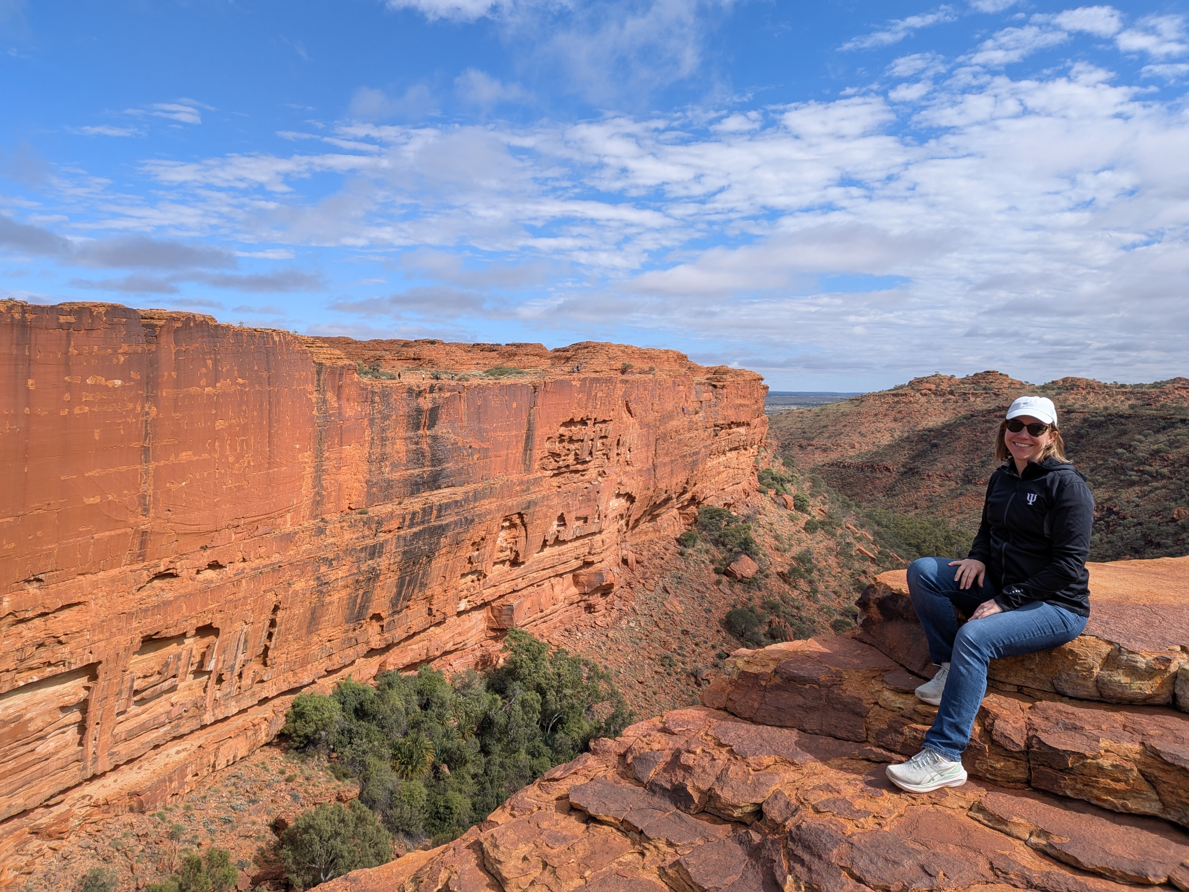 Erin sitting on the canyon edge with the cliff face behind