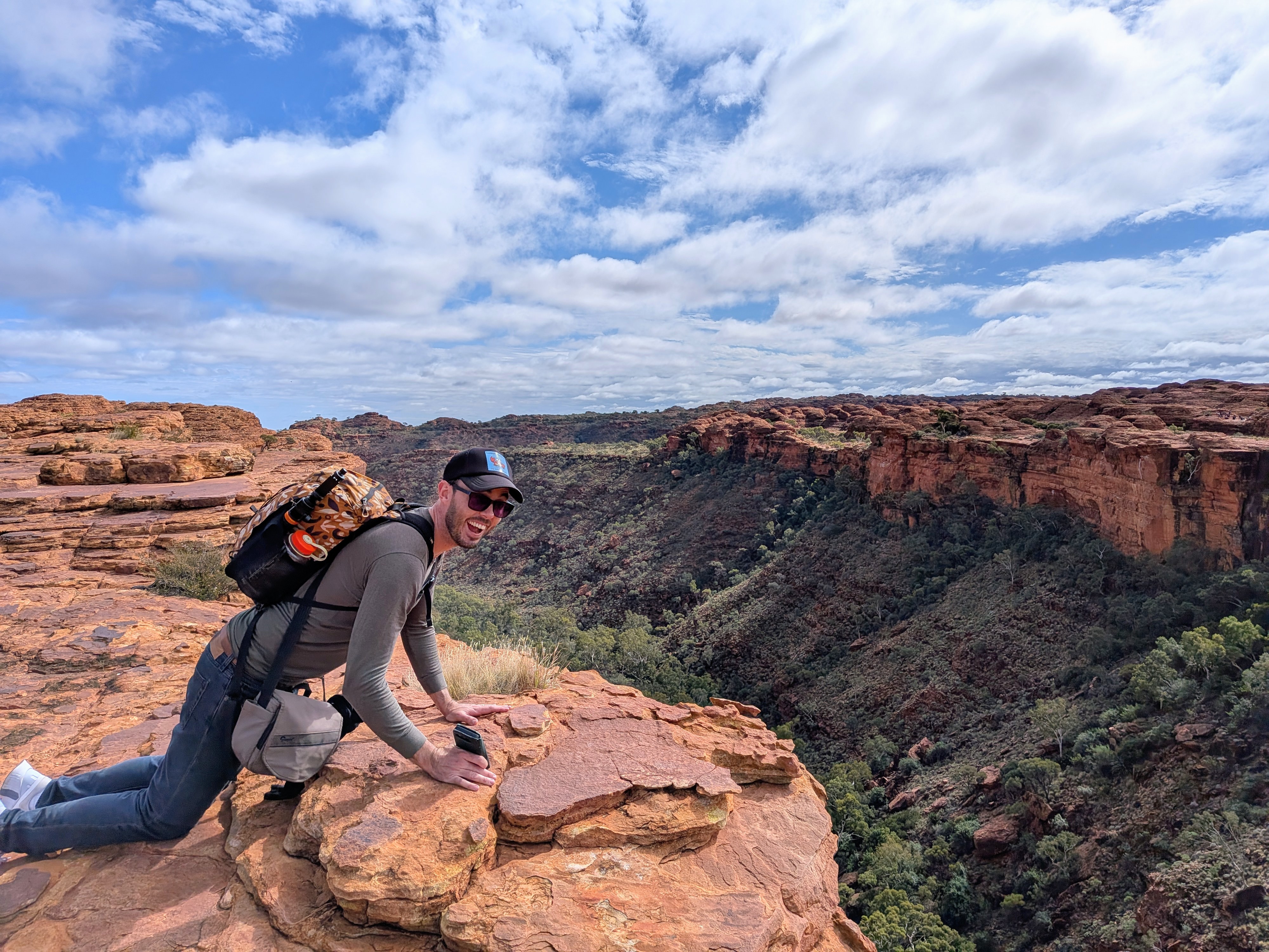 Dylan sitting on the rim edge with backpack, canyon stretching out below