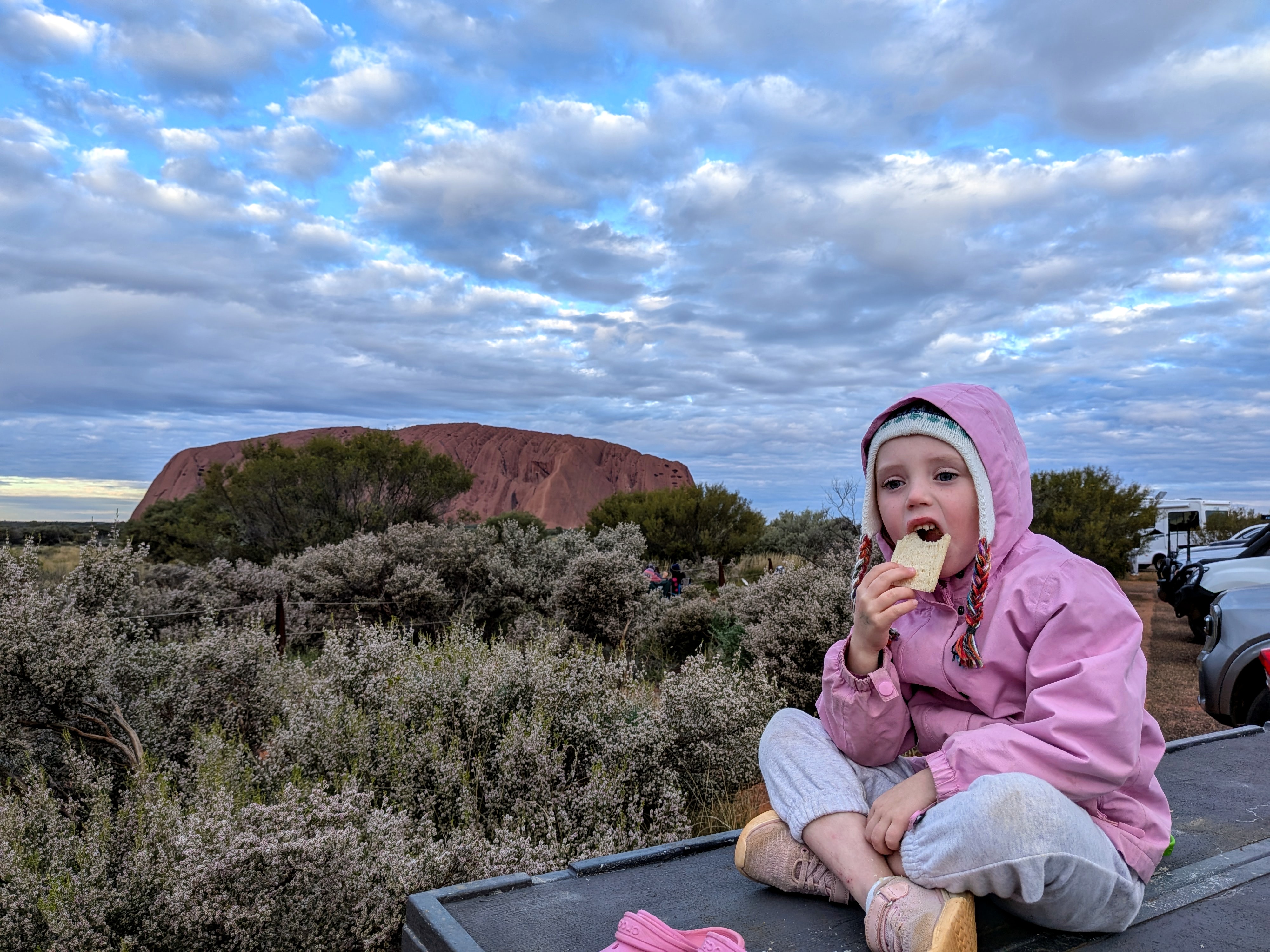 Leah eating a snack on the roof rack with Uluru behind