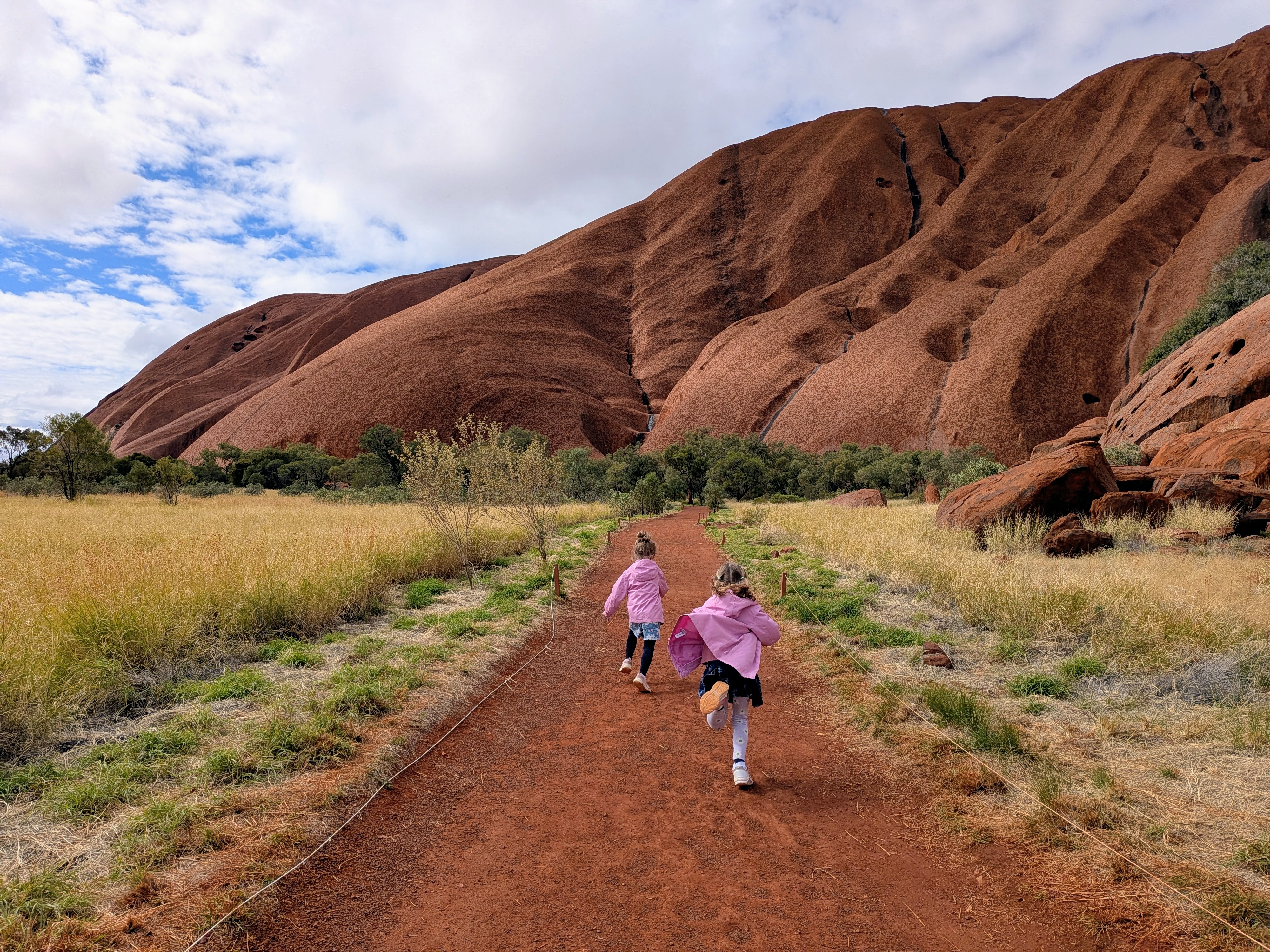 The girls running down the red path toward Uluru