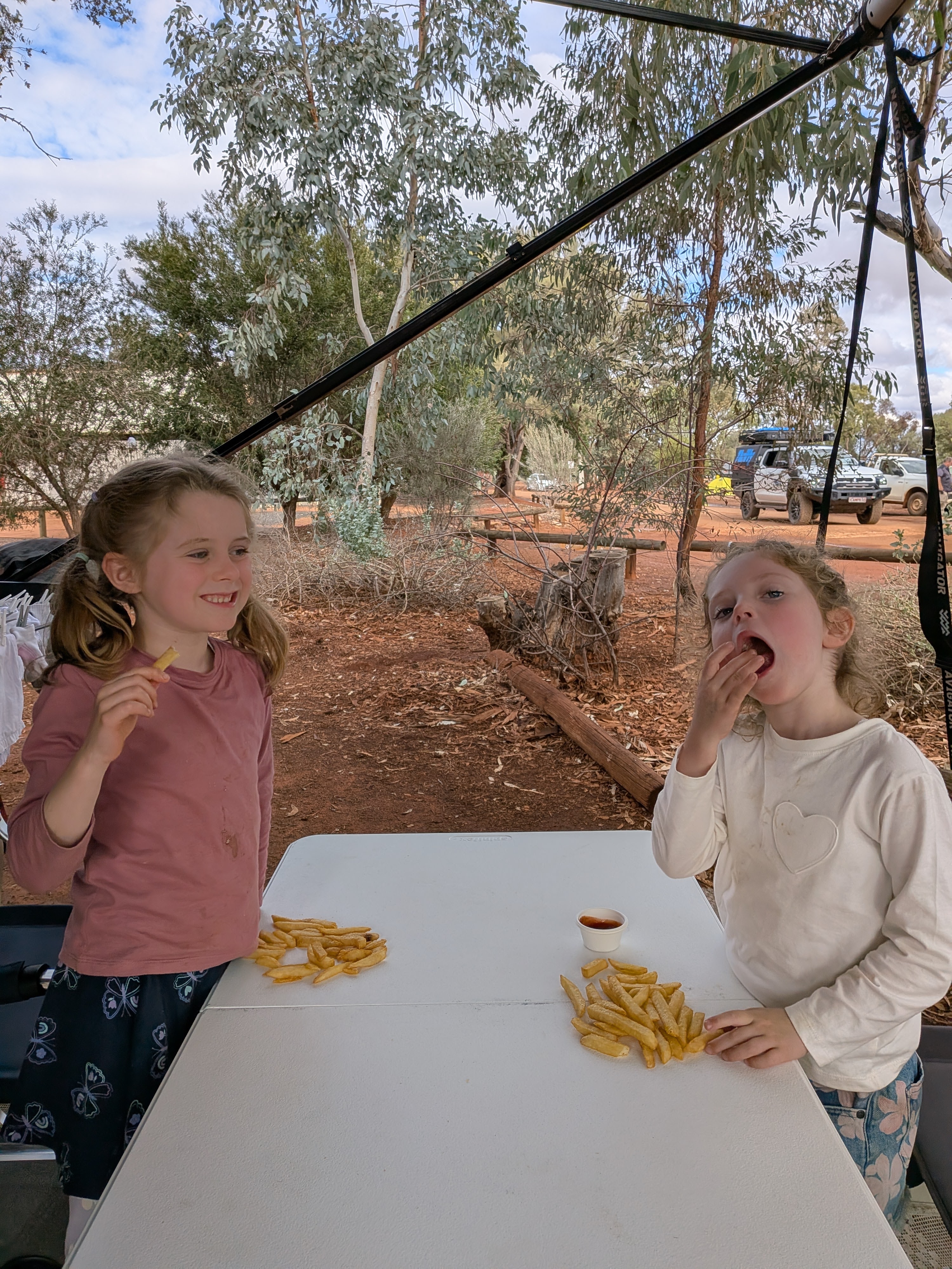 The girls eating chips under the awning at camp