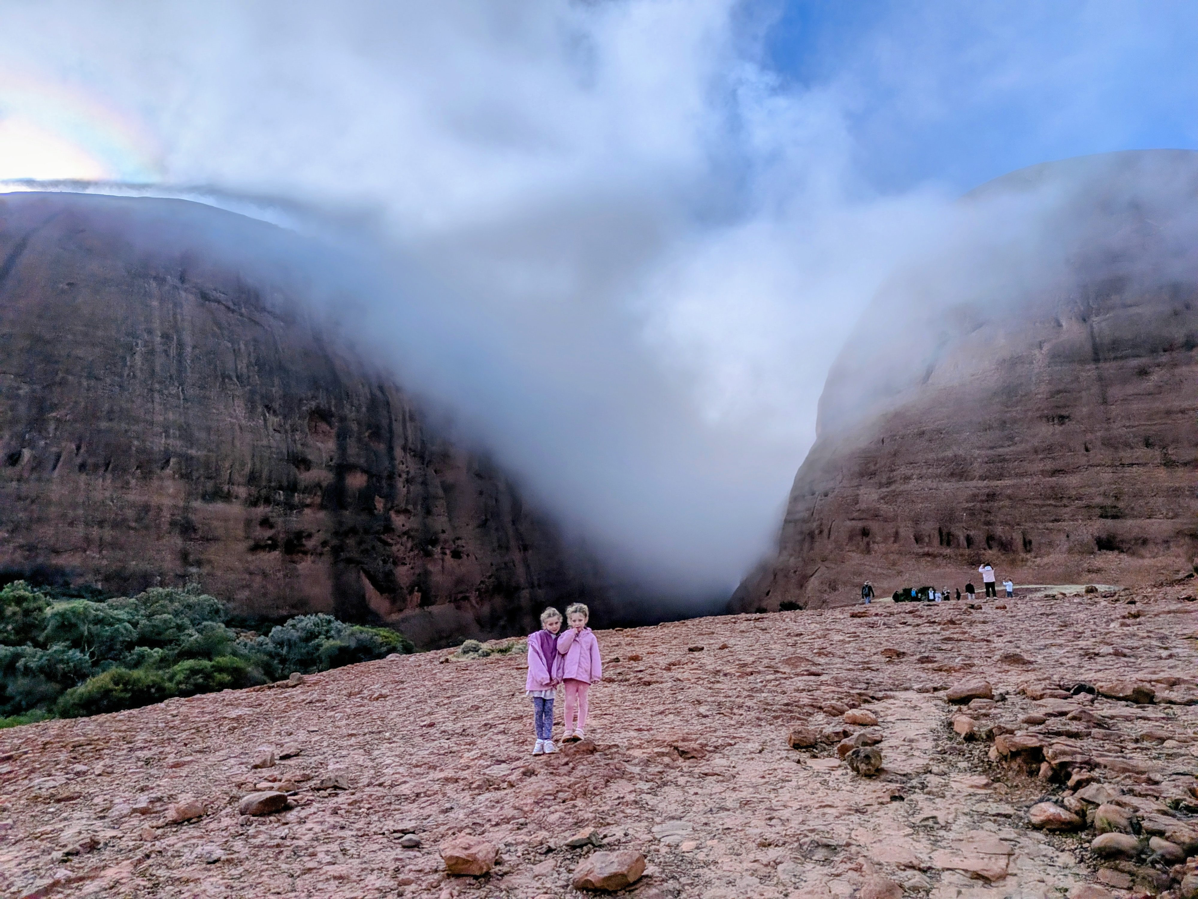The girls standing with fog-wrapped dome and a rainbow behind