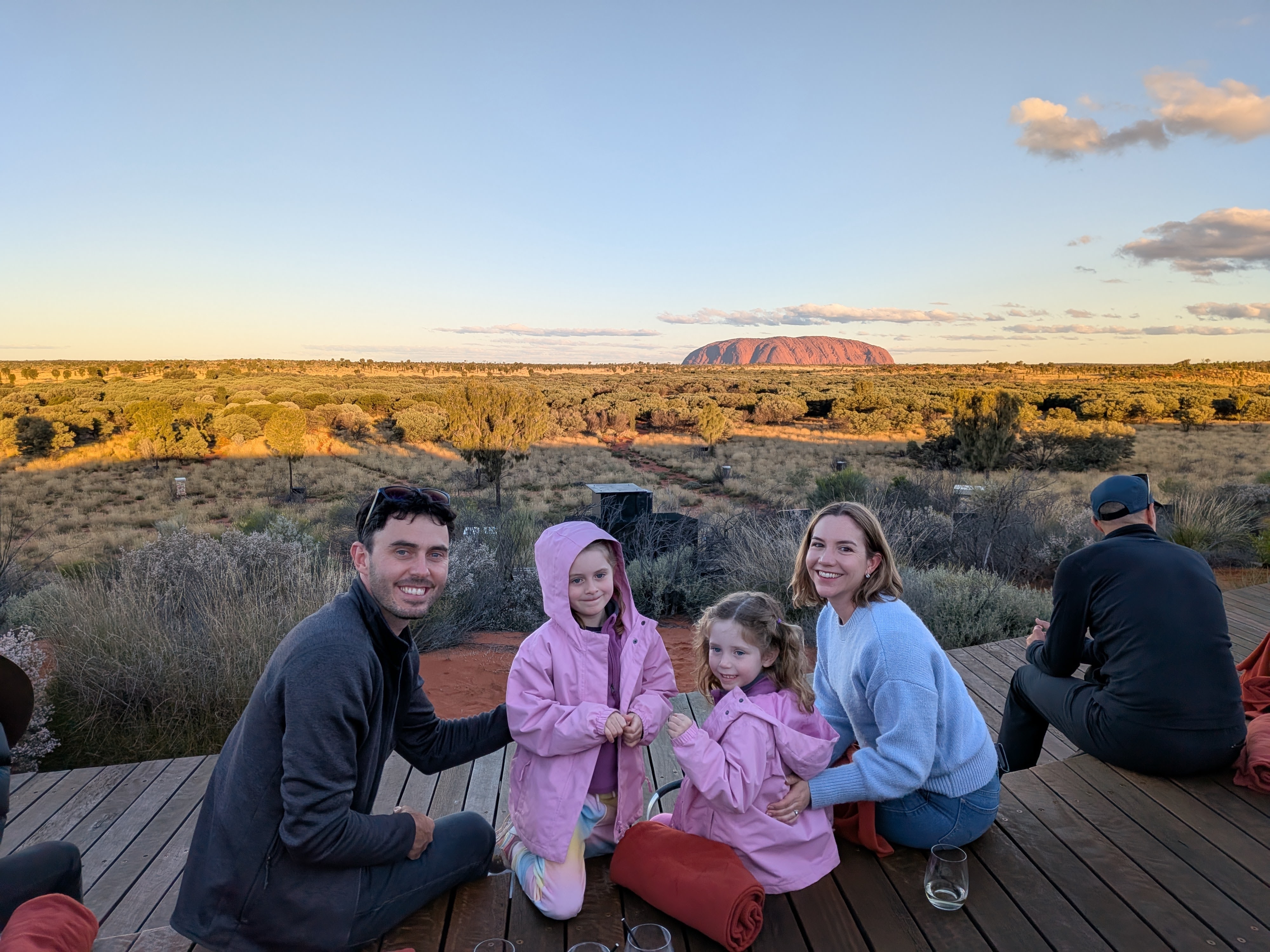Family seated on the Wintjiri Wiru deck with Uluru at sunset