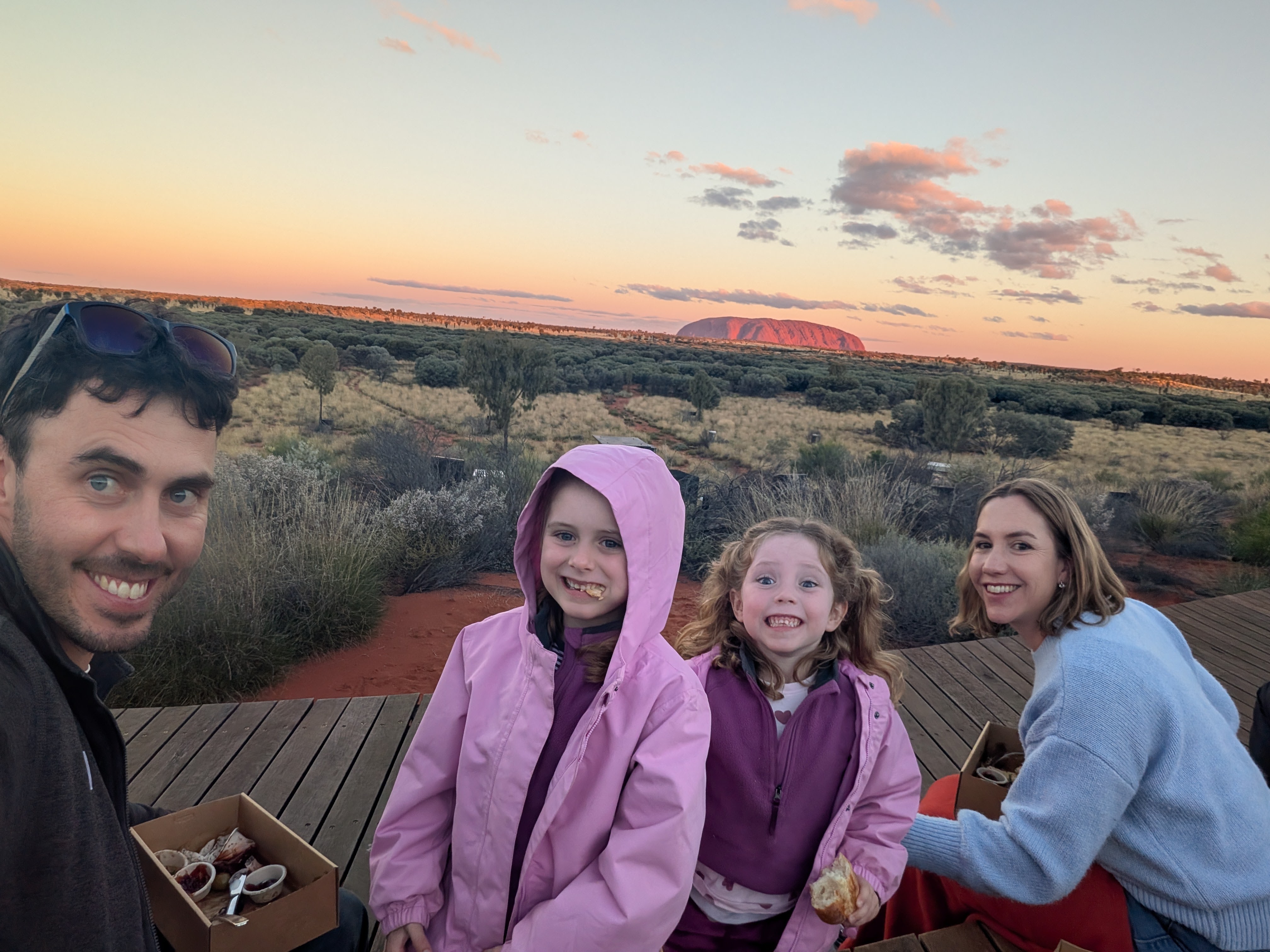 Family selfie with pink sunset sky and Uluru glowing behind