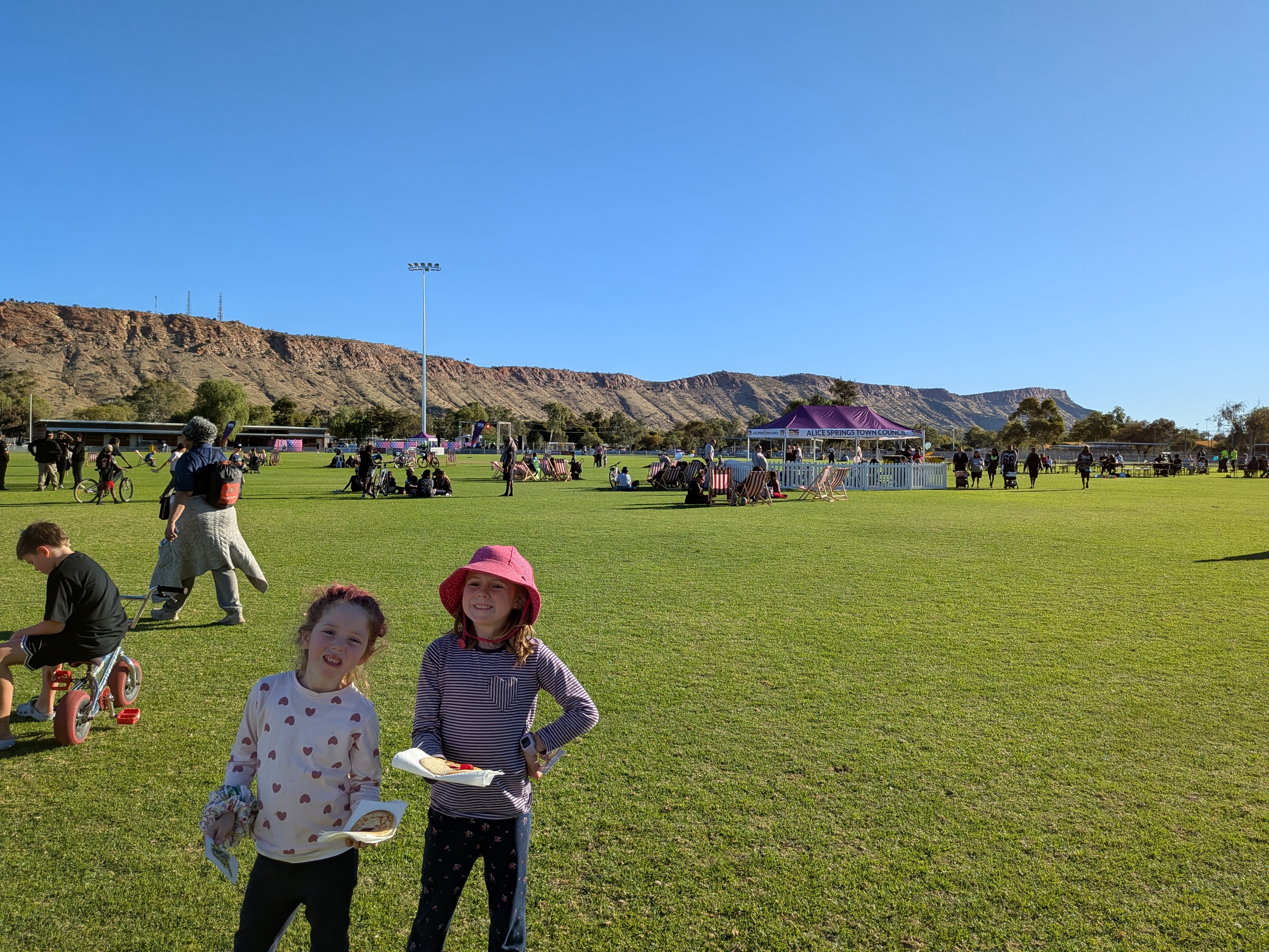 The girls with food at the Newlandia Festival with the MacDonnell Ranges behind