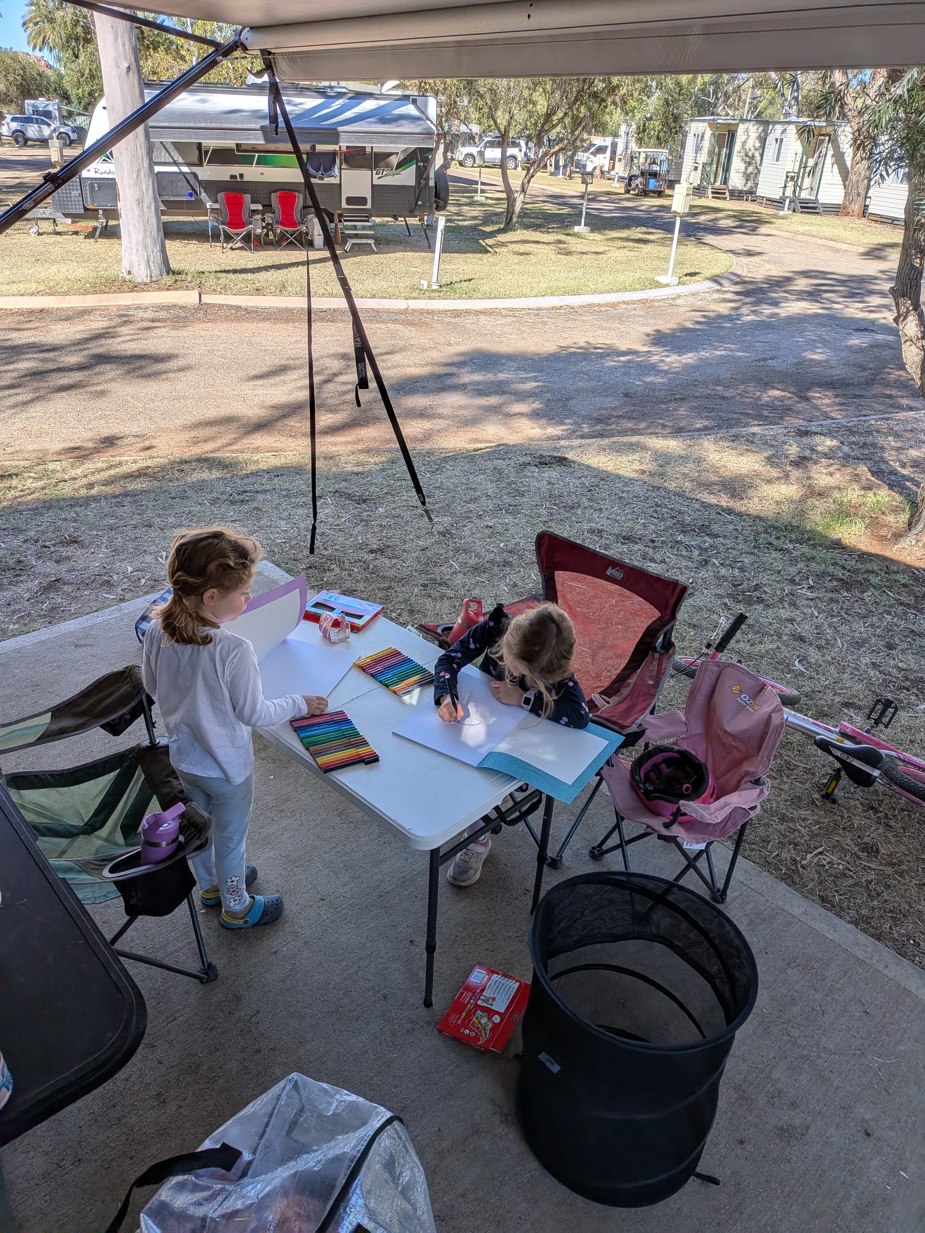 The girls drawing and colouring at the camp table in the morning sun