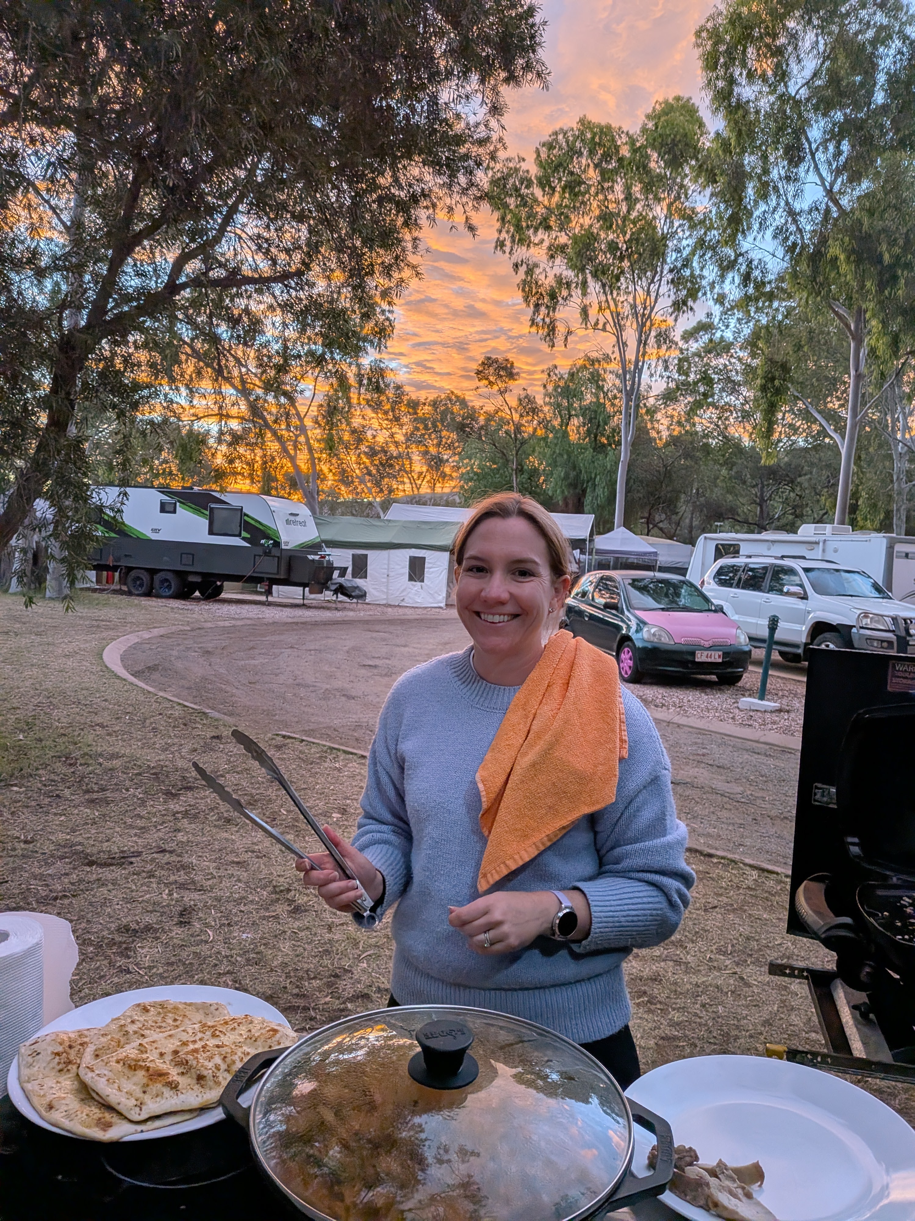 Erin cooking butter chicken at camp with a pink sunset sky behind