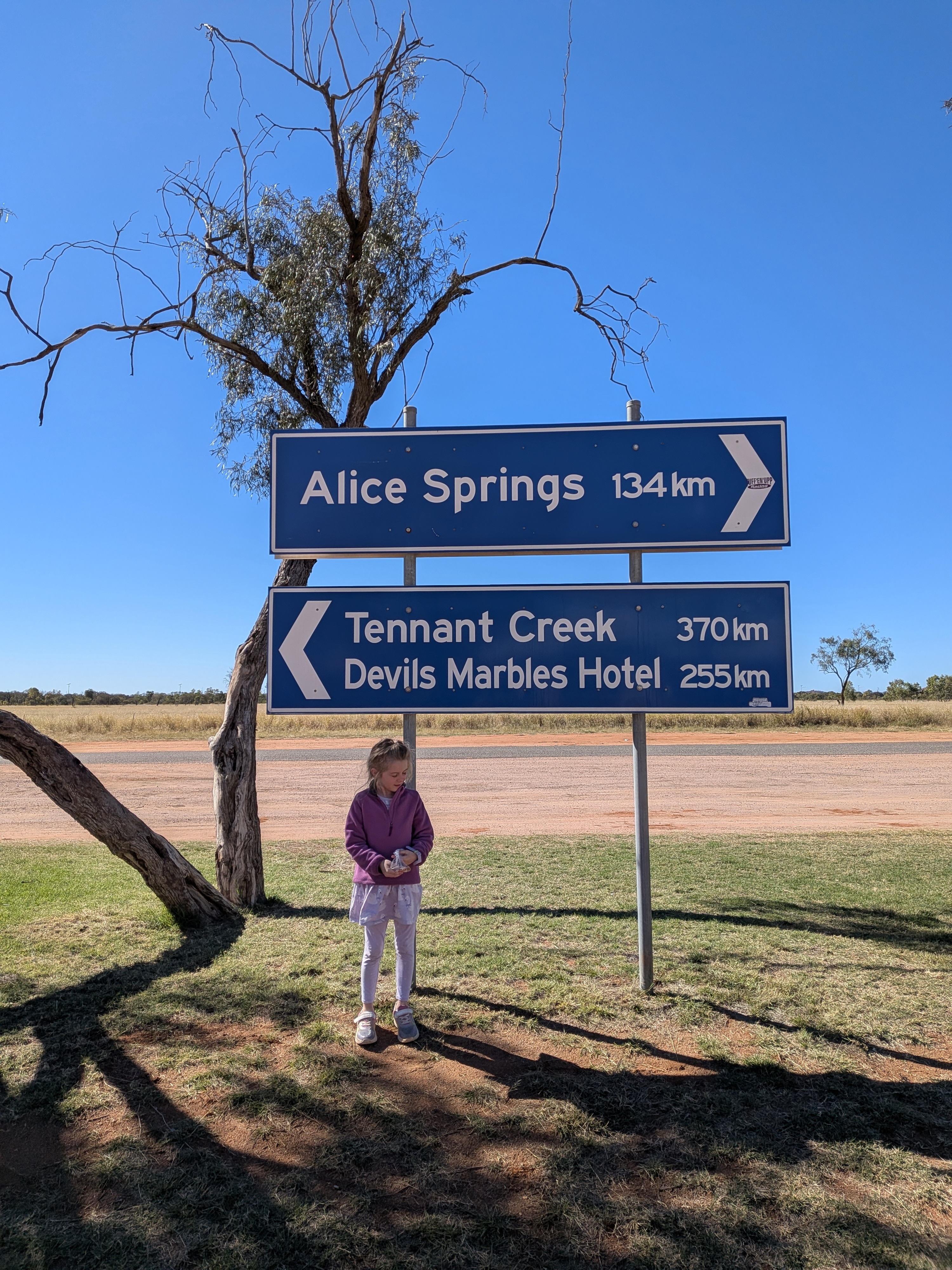 Hazel under the highway signs at Aileron, 134km back to Alice Springs and 370km on to Tennant Creek