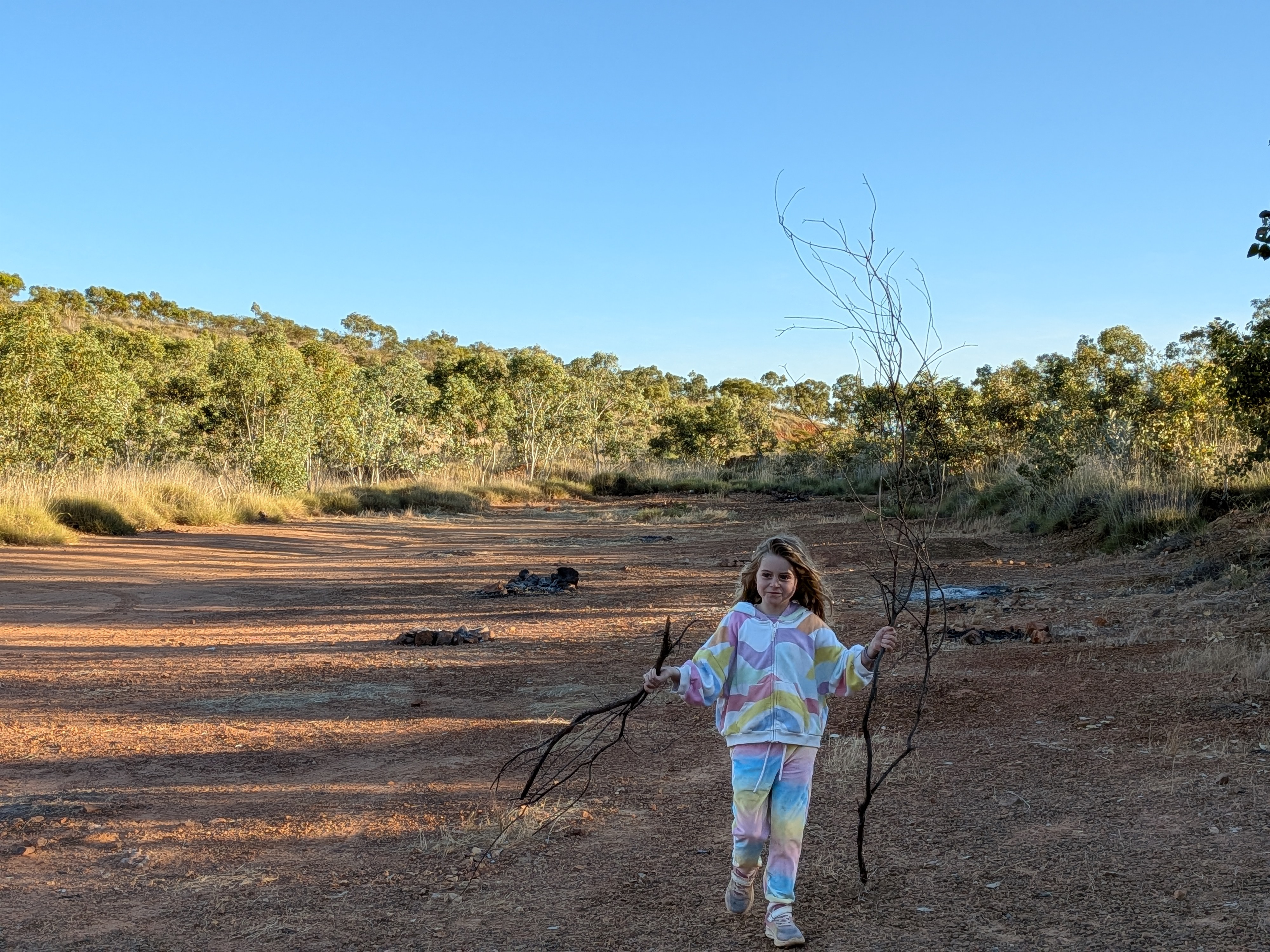 Hazel carrying branches of firewood across the red dirt at the free camp