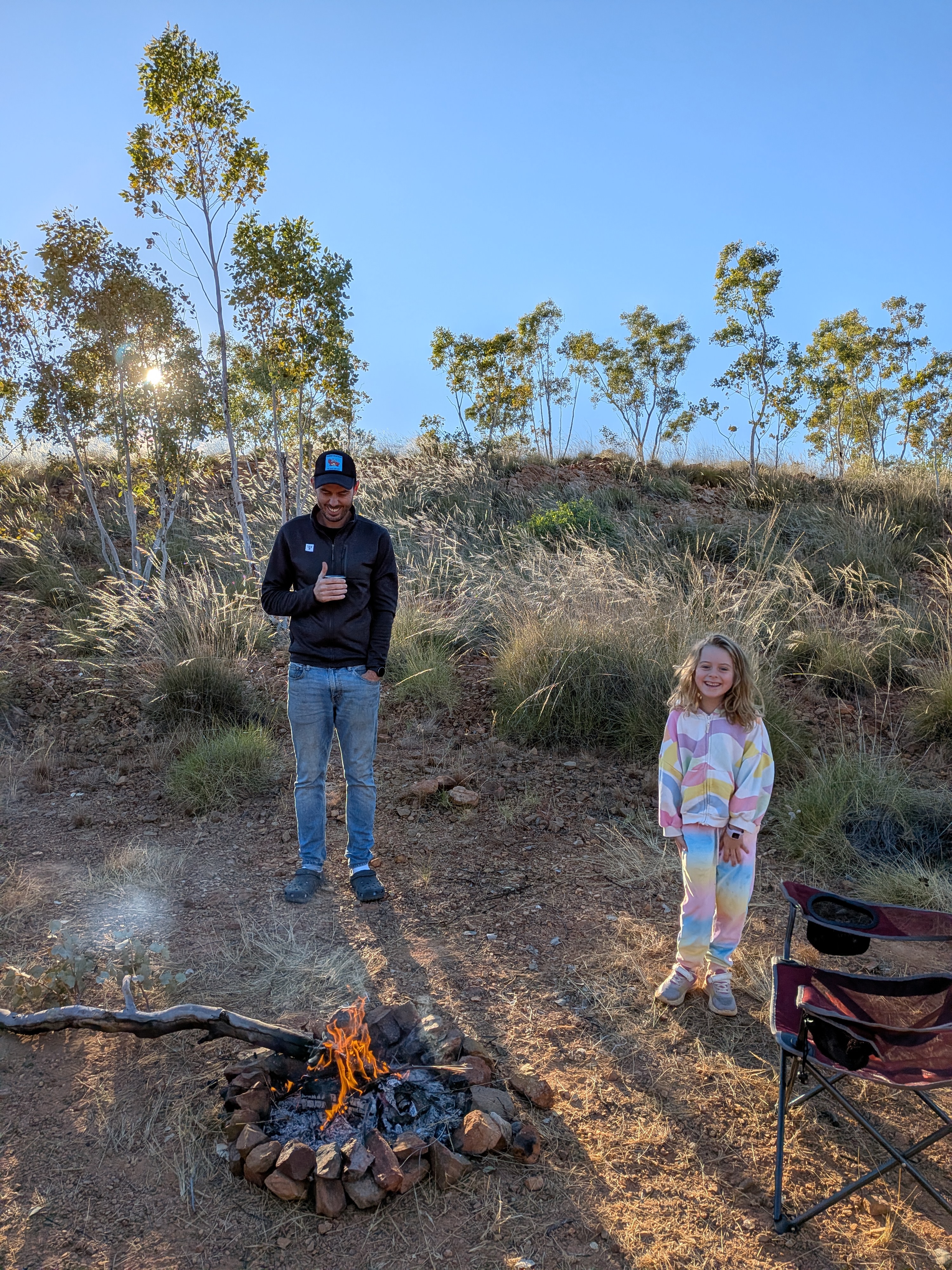 Dylan with his coffee and Hazel grinning by the morning campfire