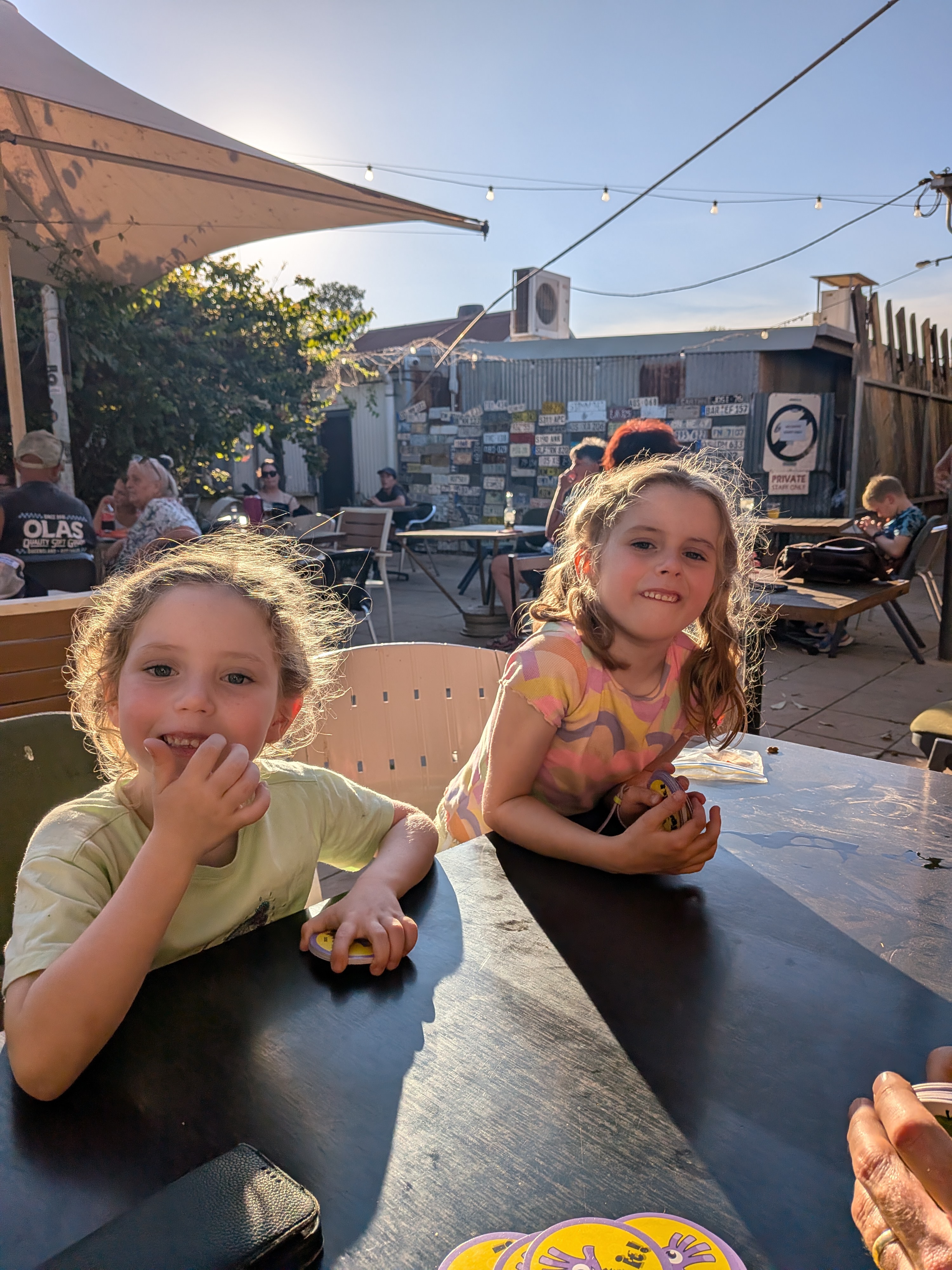 Leah and Hazel playing cards at a beer garden table in front of the number-plate wall
