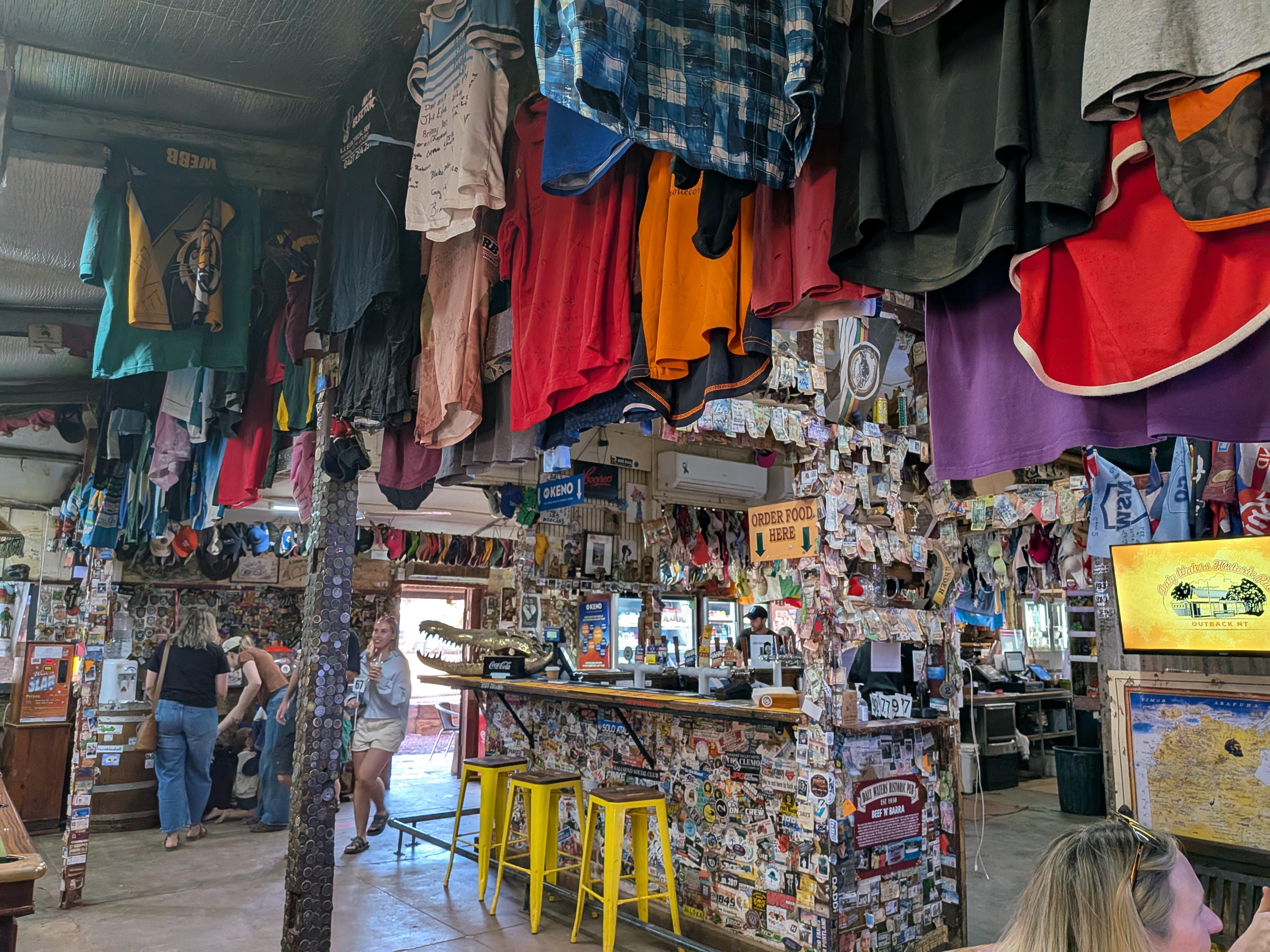 Inside the pub — hundreds of t-shirts hanging from the ceiling above the sticker-covered bar and golden croc head