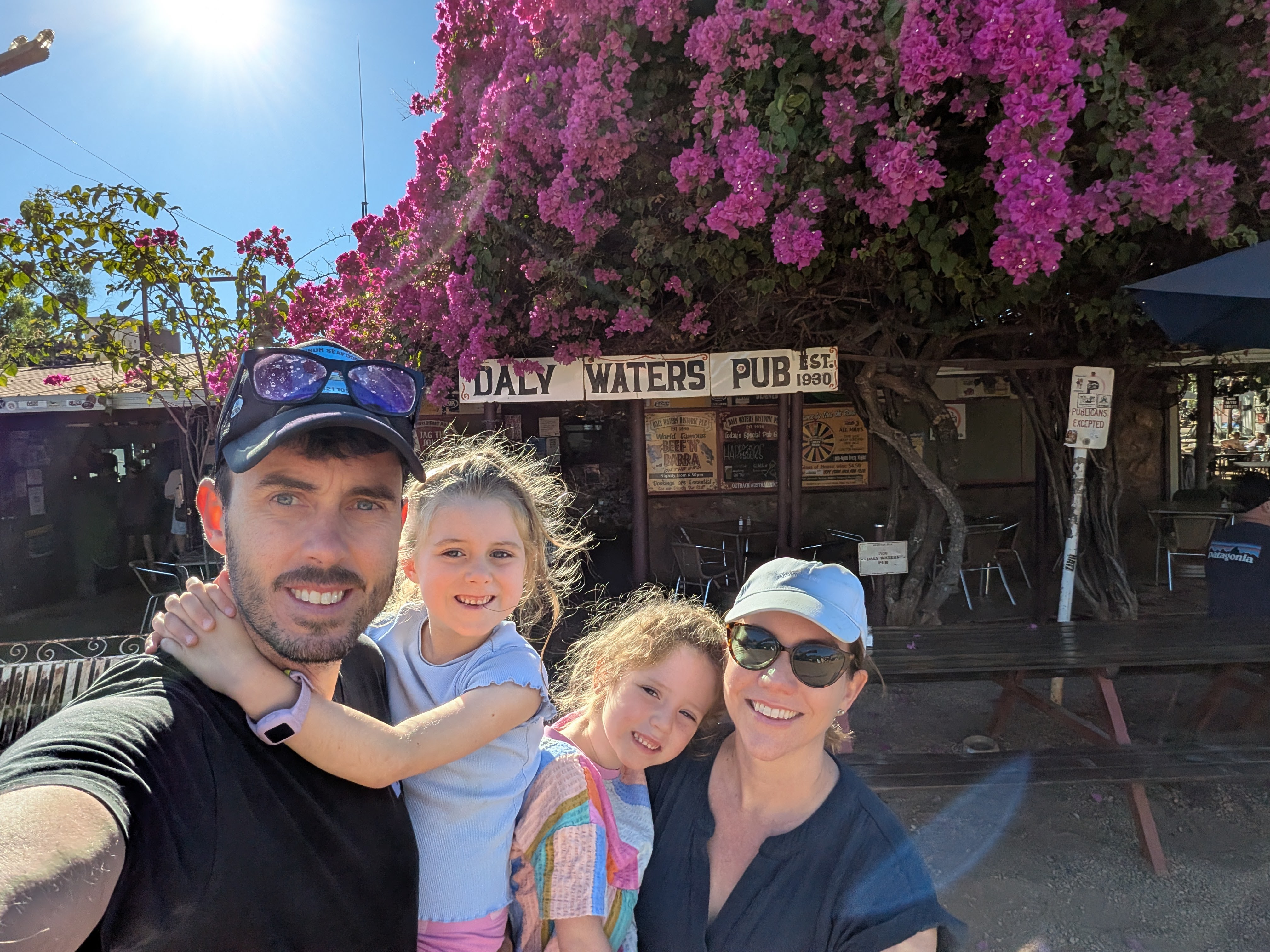 Family selfie under the bougainvillea at the Daly Waters Pub sign before setting off