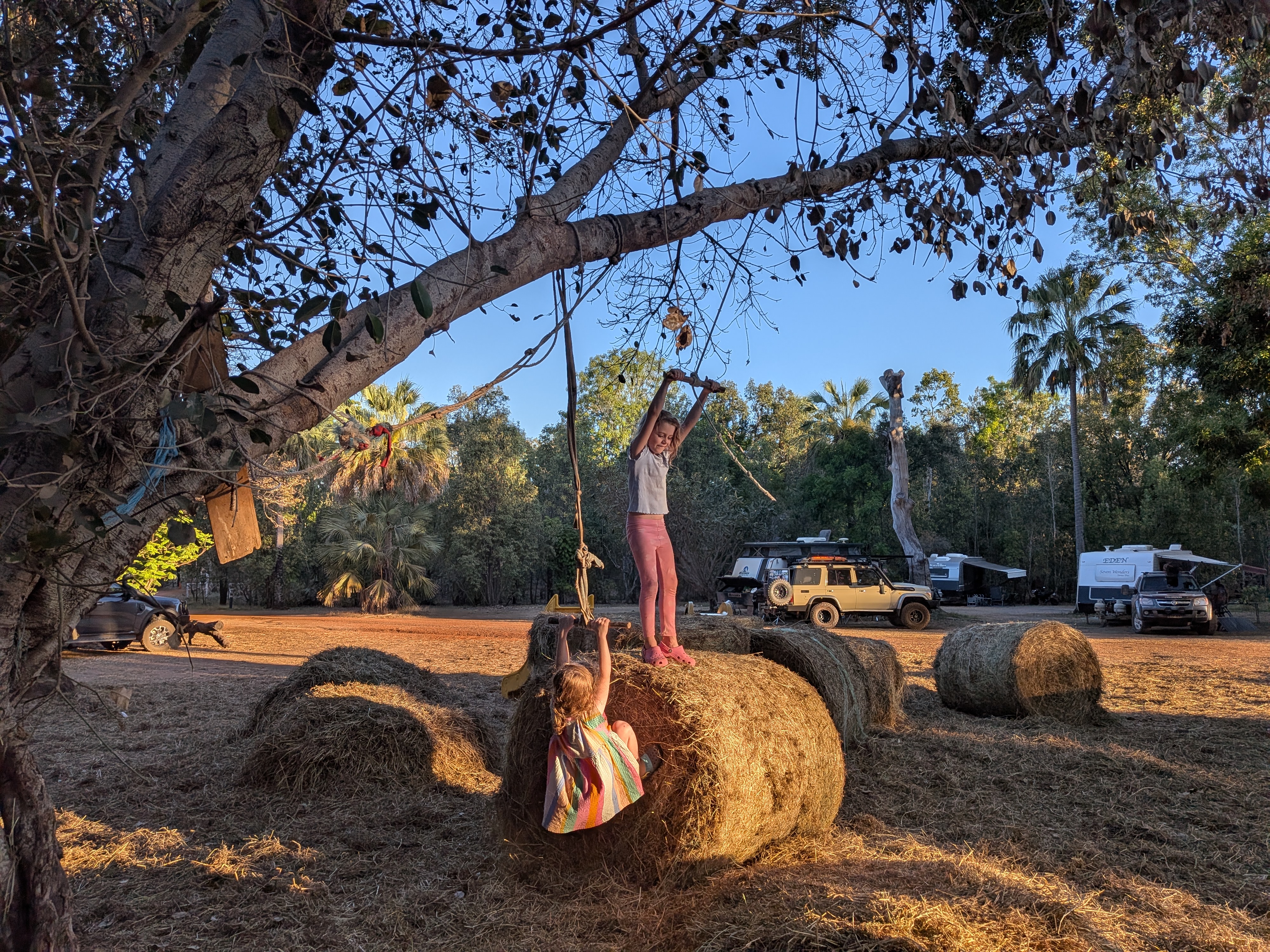 The girls climbing the hay bales under the rope-swing tree at golden hour