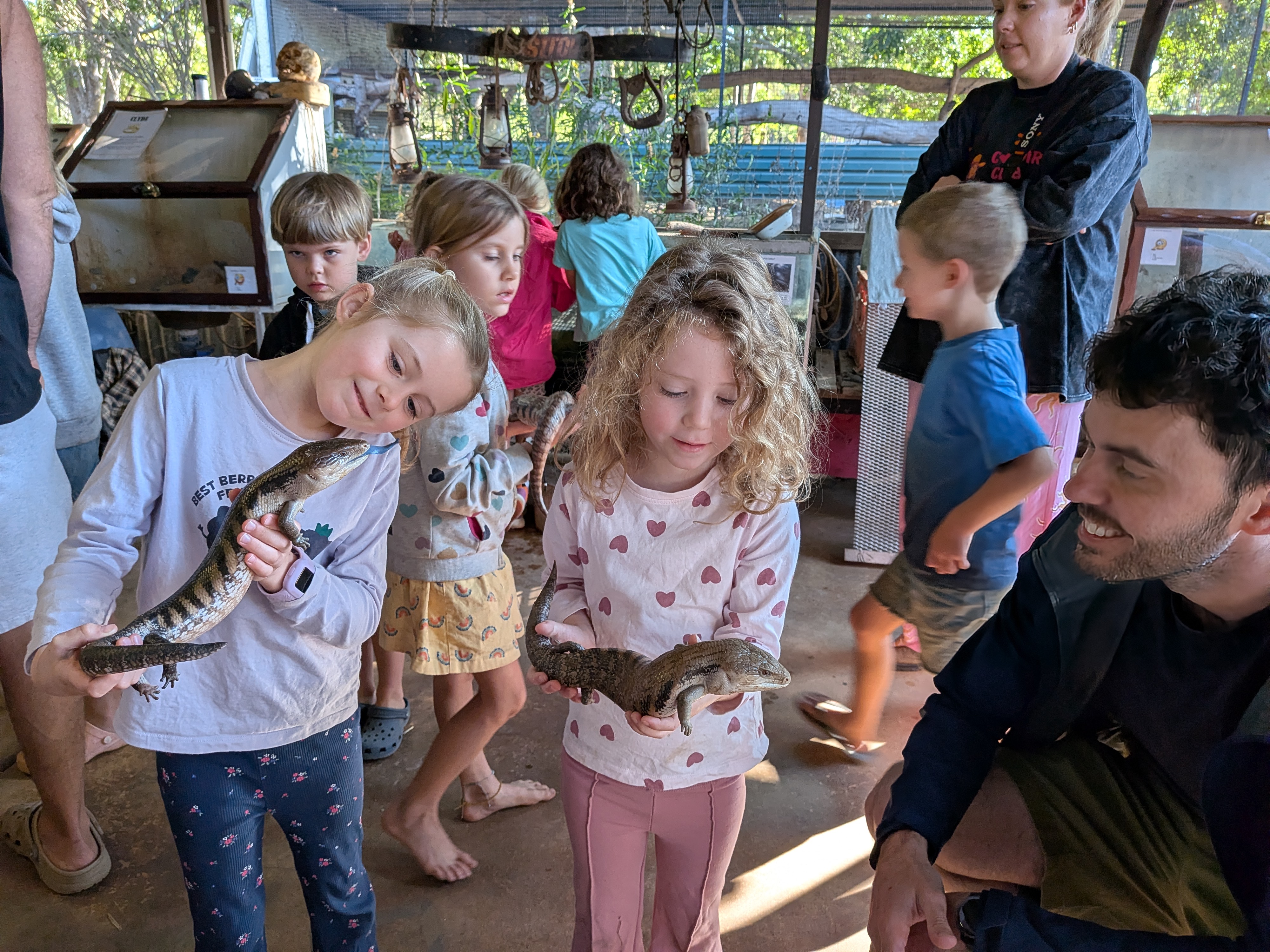 Hazel and Leah each holding a blue-tongue lizard while Dylan looks on