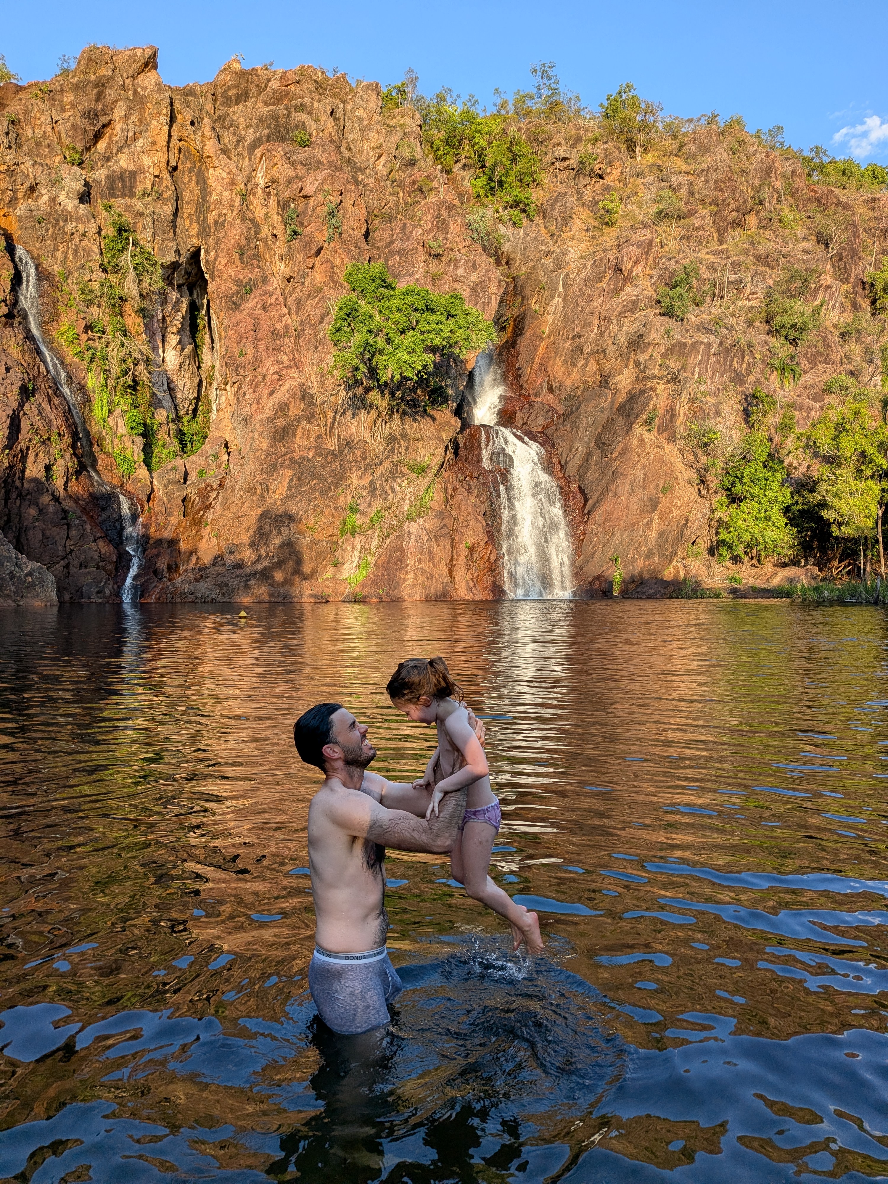 Dylan lifting Leah out of the water mid-laugh, the cliff glowing behind them