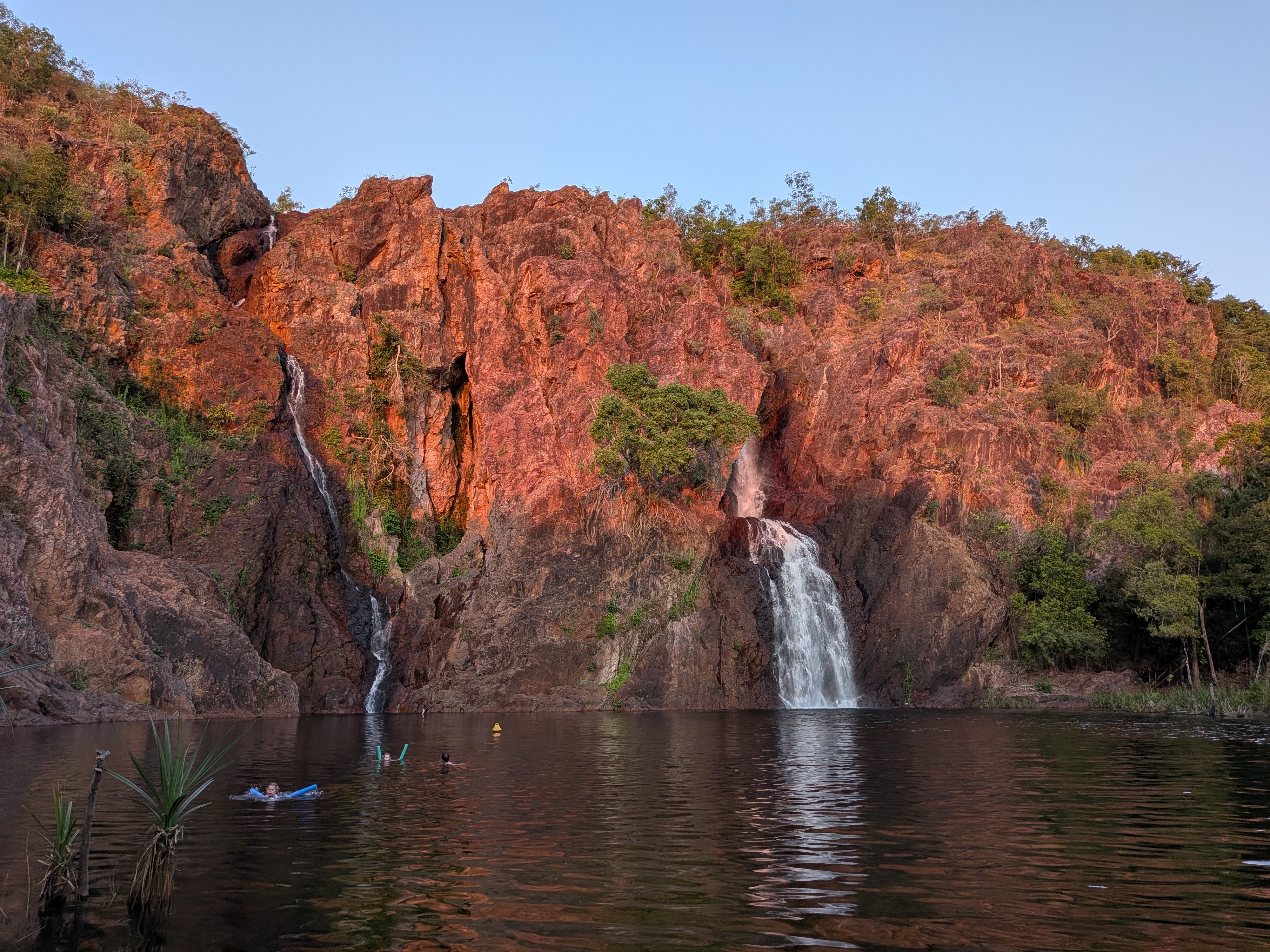 Sunset over Wangi Falls, swimmers tiny in the plunge pool