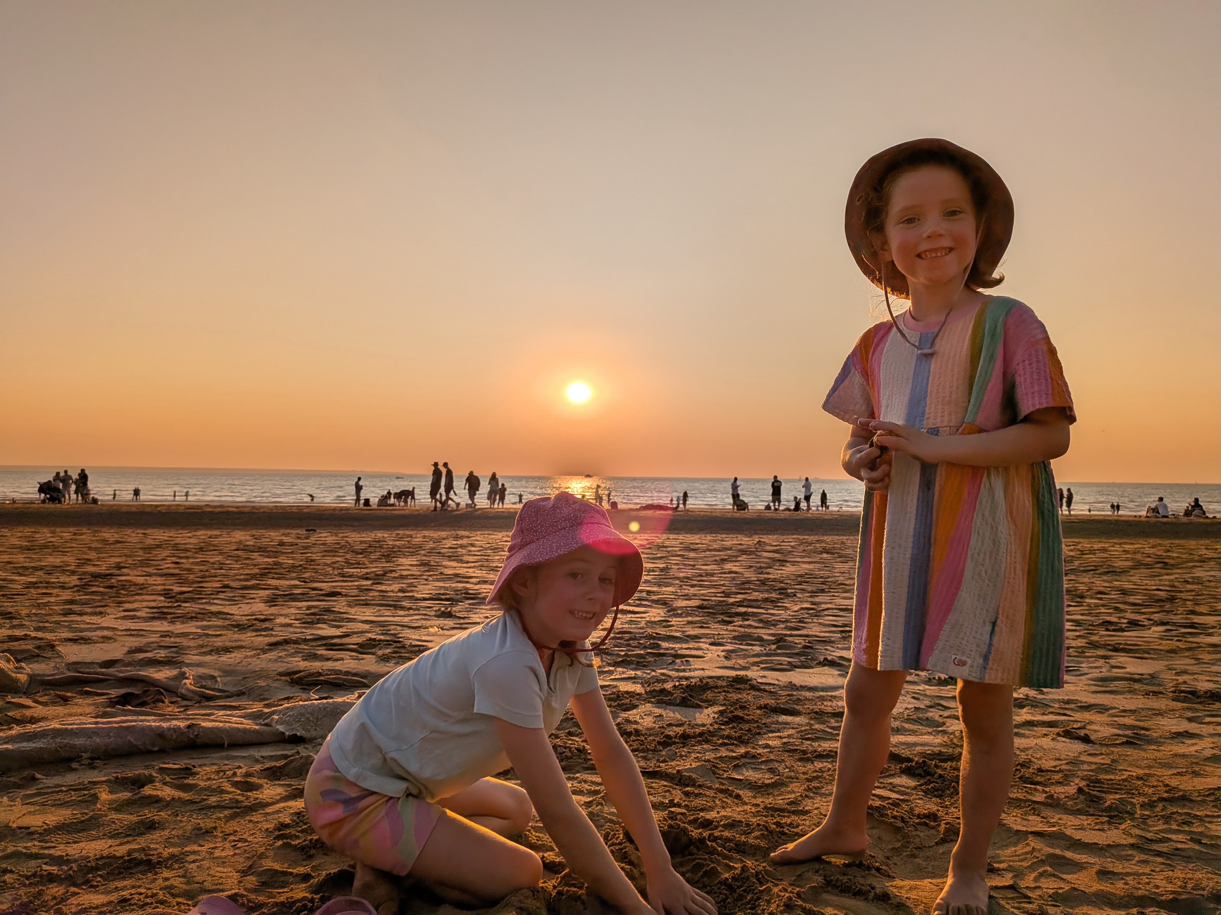 Hazel and Leah digging in the sand as the sun sets over Mindil Beach