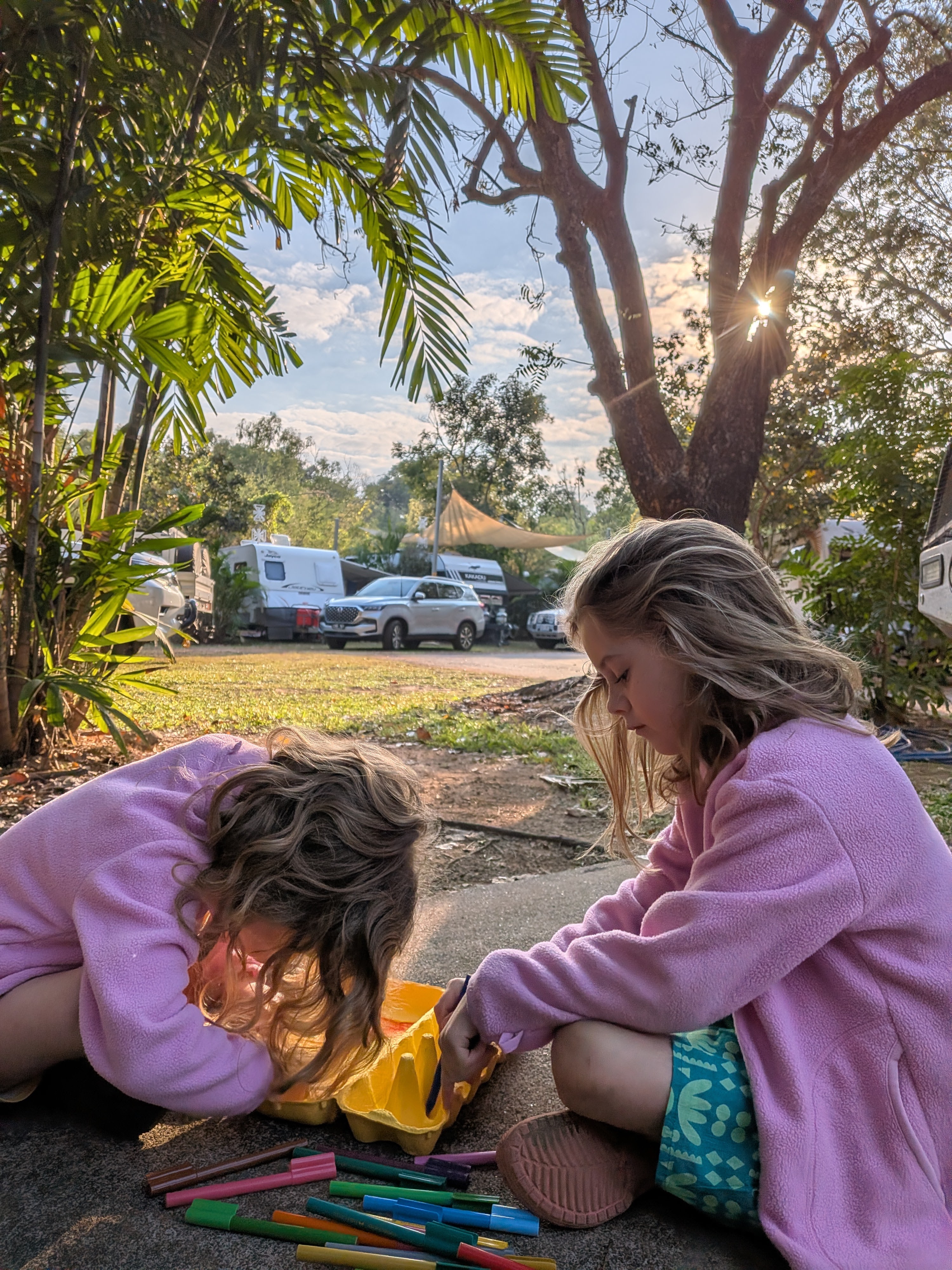 Hazel and Leah in matching fleeces colouring an egg carton in the morning sun at the campsite