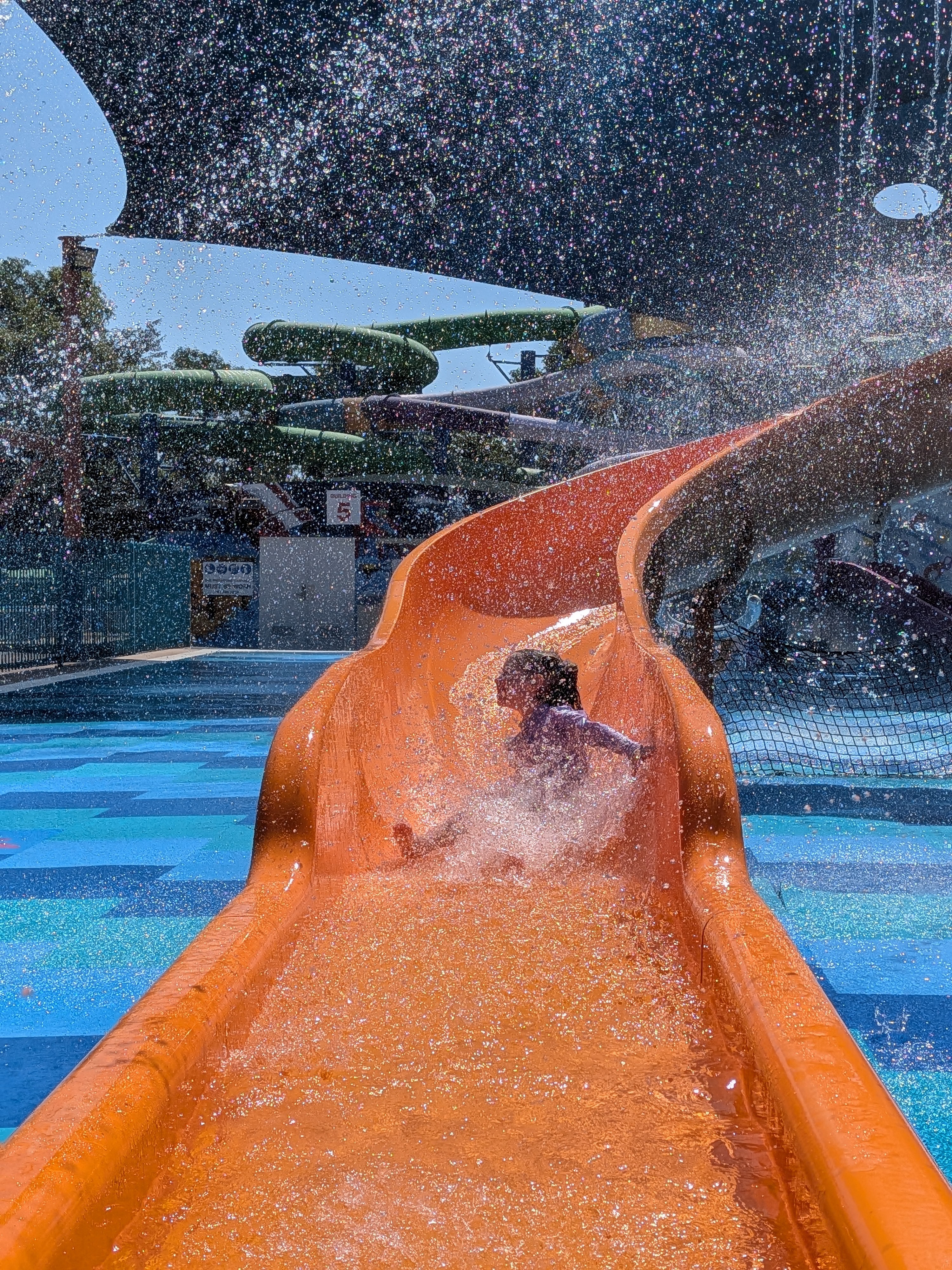 Bursting through the backlit spray on the orange slide at Leanyer Recreation Park