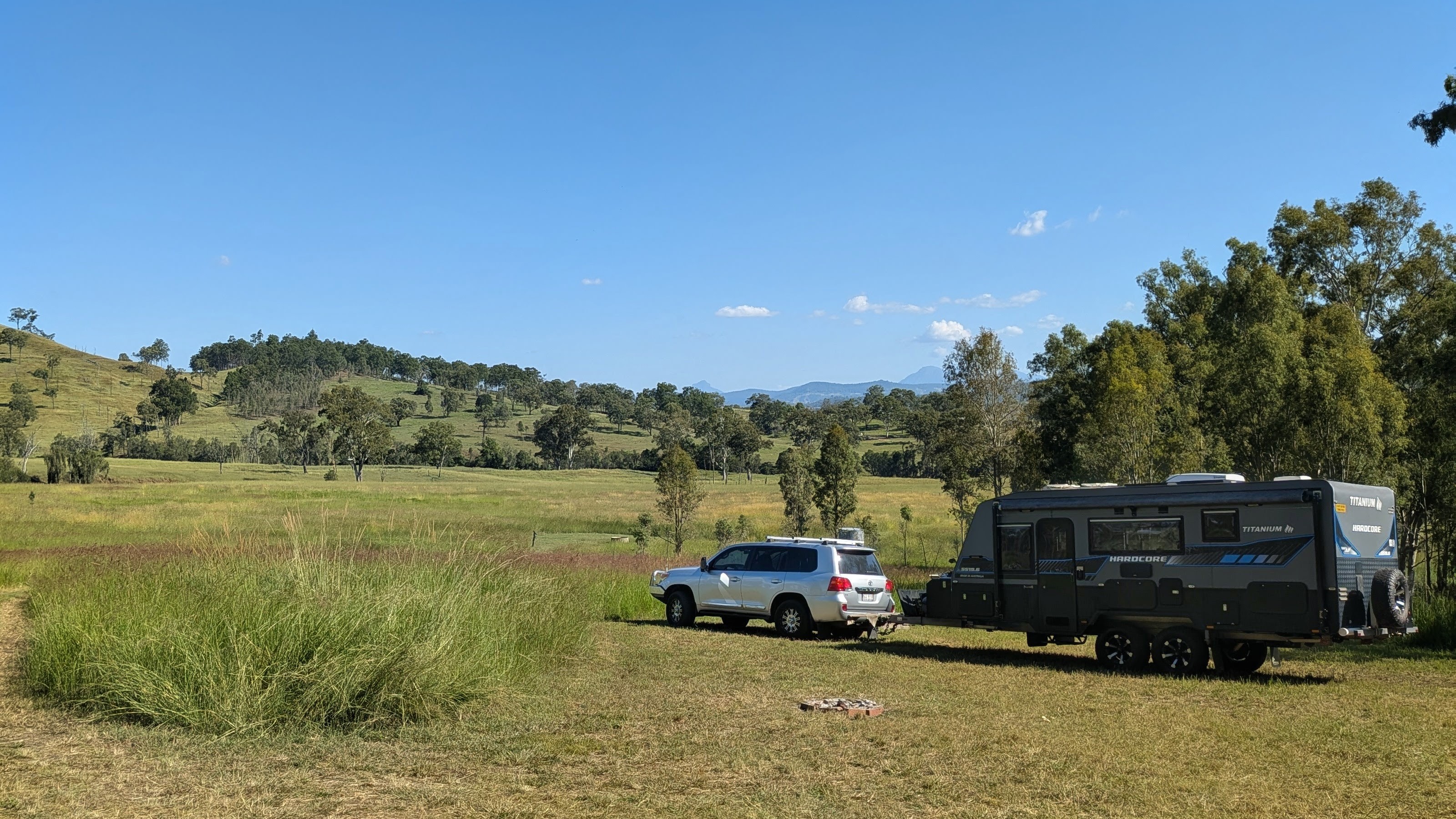 Reg the Landcruiser hitched to the TITANIUM HARDCORE caravan in a grassy paddock with hills behind